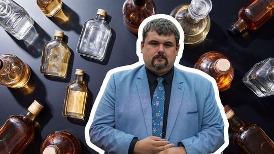 mężczyzna w garniturze na tle małych butelek z alkoholem