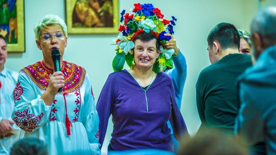 zdjęcie przedstawia kobietę w wianku na głowie, obok druga kobieta trzyma mikrofon