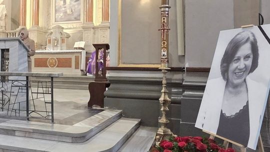 zdjęcie przedstawia wnętrze kościoła, na posadce stoi portret kobiety, w głębi ołtarz i stojąca kobieta przy pulpicie