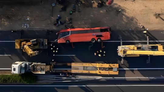 autobus leżący na boku między dzwigami