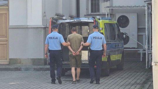 zdjęcie przedstawia policjantów prowadzących zatrzymanego, w kajdankach, przed radiowozem