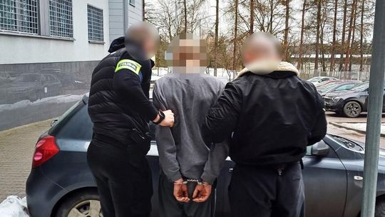 zdjęcie przedstawia mężczyznę z kajdankach prowadzonego przez innych mężczyzn