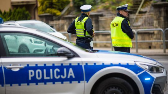 Zdjęcie przedstawia radiowóz policyjny na tle policjantów