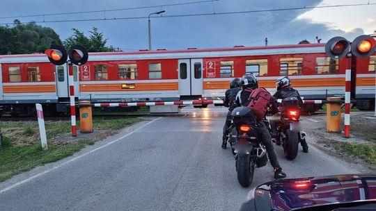 zdjęcie przedstawia pociąg przejeżdżający przez przejazd kolejowy, przed którym stoją motocykle