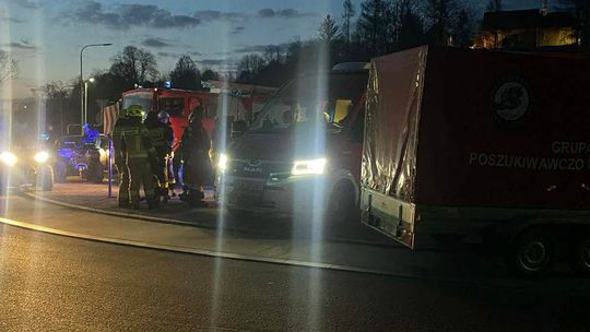 zdjęcie przedstawia strażaków obok samochodów straży pożarnej w nocy