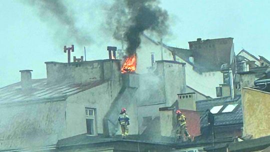 strażacy na dachu budynku z którego okna wydobywa się ogień i dym