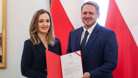 zdjęcie przedstawia kobietę i mężczyznę trzymających czerwoną teczkę