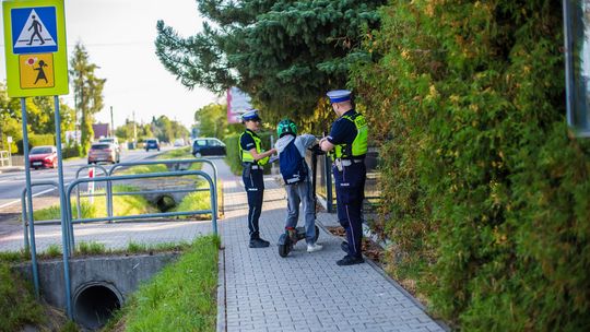 policjanci rozmawiają z chłopakiem, który przyjechał do szkoły na hulajnodze
