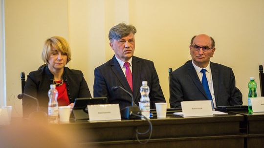zdjęcie przedstawia dwóch mężczyzn i kobietę w garniturach przy stole