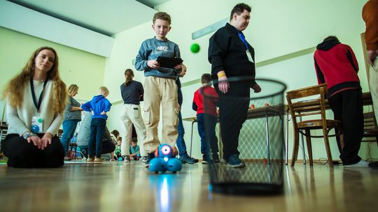 zdjęcie przedstawia chłopca który trzyma tablet sterujący robotem, obok siedzi dziewczyna