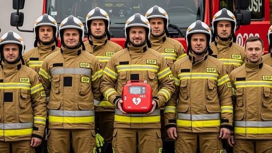 zdjęcie przedstawia strażaków w mundurach trzymających urządzenie AED