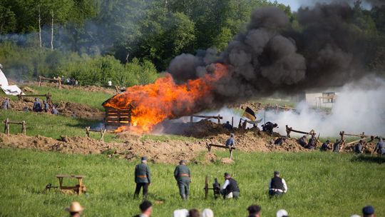 żołnierze na polu walki rekonstrukcji historycznej w Sękowej, w tle palący się dom