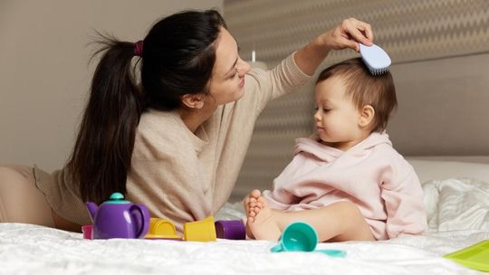 mama leży z dzieckiem na łóżku i czesze dziecku główkę grzebieniem