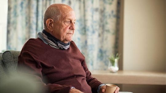 zdjęcie przedstawia starszego mężczyznę siedzącego na fotelu w domu