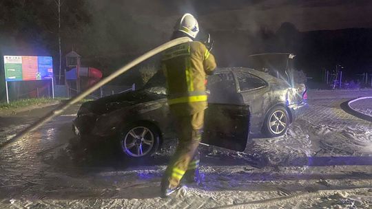 strażak z wężem na plecach polewa spaloną karoserię pojazdu, zdjęcie w noc z Siar