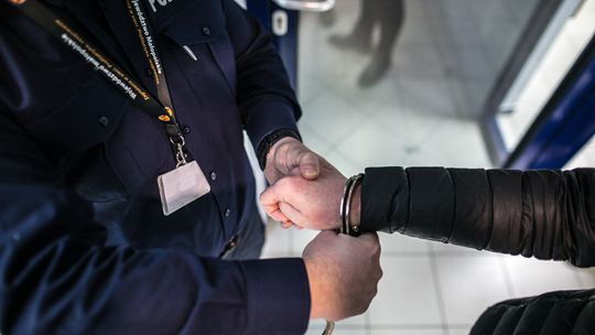 ręka policjanta zakładająca kajdanki na inną rękę