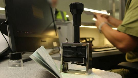 zdjęcie przedstawia pieczątkę na biurku w tle paszport i mężczyzna w mundurze