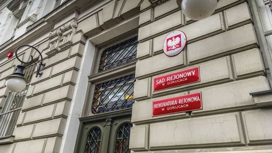 zdjęcie przedstawia drzwi wejściowe do budynku prokuratury w Gorlicach, obok drzwi czerwone tabliczki z szyldami instytucji