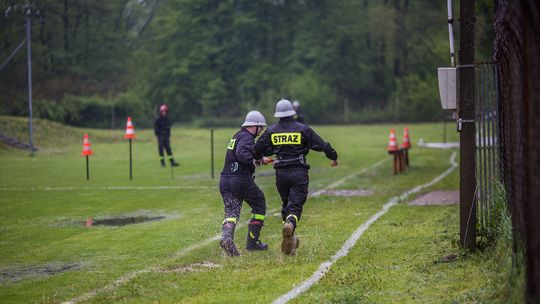 zdjęcie przedstawia biegnących strażaków podczas zawodów, pod ich nogami rozpryskuje woda z kałuży