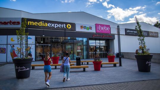 zdjęcie przedstawia wejście do galerii gorlickiej, przed którą stoją ławeczki i donice z roślinami