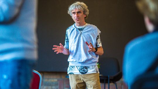zdjęcie przedstawia mężczyznę który mówi do ludzi i rozkłada ręce