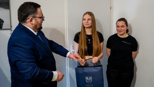 zdjęcie przedstawia dwie kobiety i mężczyznę, który wręcza im prezent