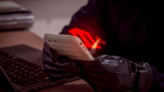 mężczyzna w czarnych rękawiczkach trzymający telefon, wyświetlają się mu na ubraniu czerwone znaki