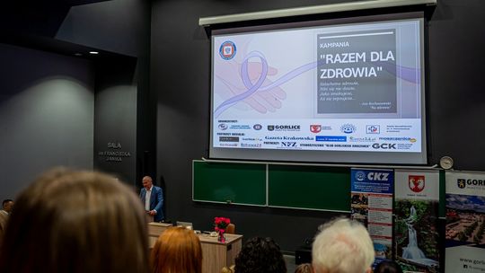 zdjęcie przedstawia ekran na ścianie, przed nim siedzą osoby na audytorium