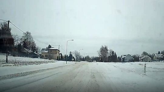 zdjęcie przedstawia śnieg zalegający na jezdni i polach, w tle zabudowania