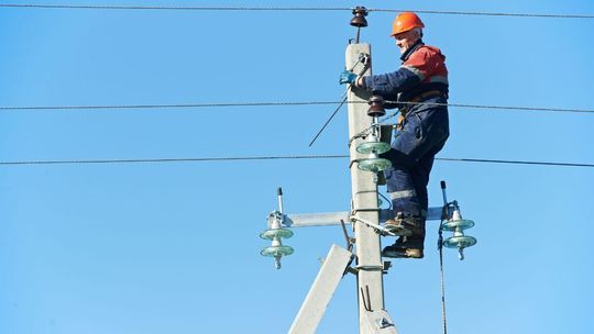 zdjęcie przedstawia mężczyznę na słupie energetycznym w kasku