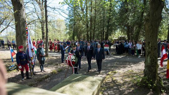 zdjęcie przedstawia kilku mężczyzn w garniturach składających wieniec na cmentarzu
