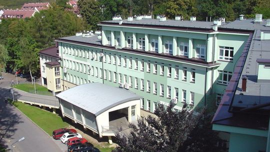 zdjęcie przedstawia duży budynek szpitala w Jaśle o zielonej elewacji, przed którym stoją samochody