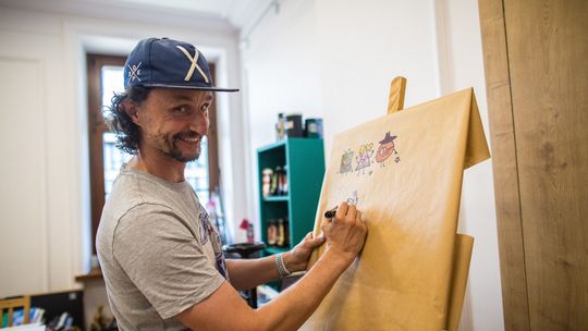 mężczyzna w czapeczce rysujący na tablicy komiks w gorlickim cenrtum kultury