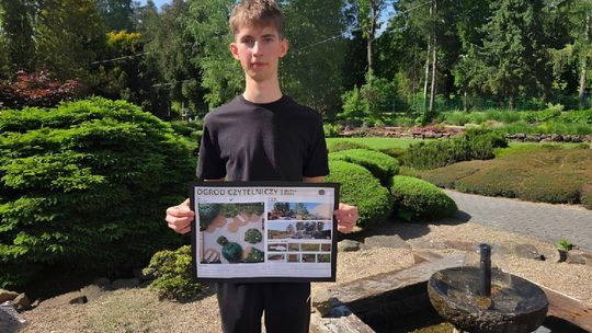 zdjęcie przedstawia portret młodego chłopaka, który trzyma przed sobą planszę, za nim jest ogród z zielenią