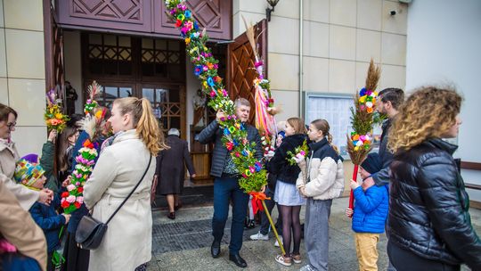 zdjęcie przedstawia mężczyznę wynoszącego palmę wielkanocną z kościoła