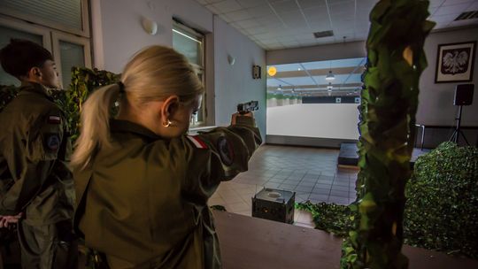 zdjęcie przedstawia dziewczynę w mundurze, która celuje do tarczy z wirtualnej broni