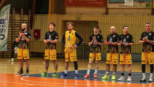 Walka o 2. ligę koszykówki trwa. Jakie wyniki półfinałów? zdjęcie przedstawia grupę sportowców w jednolitych koszulkach stojących na parkiecie pod koszem