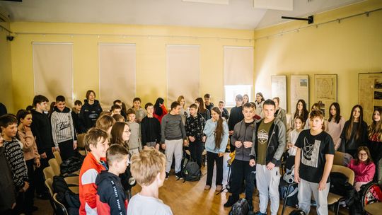 zdjęcie przedstawia stojących uczniów klas siódmych w klasie szkolnej