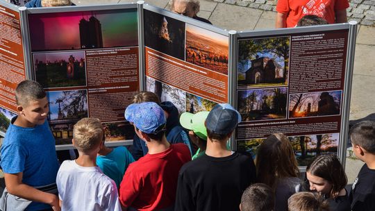 zdjęcie przedstawia tablicę ze zdjęciami przed którą jest grupa młodych osób