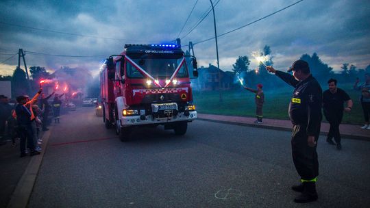 zdjęcie przedstawia samochód strażacki obok strażak z racą