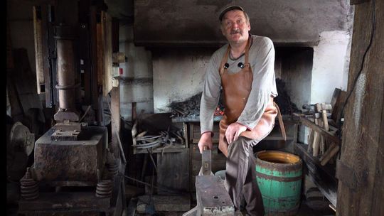 zdjęcie przedstawia mężczyznę z młotkiem i kowadłem w kuźni
