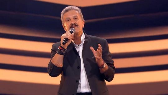 zdjęcie przedstawia mężczyznę w marynarce z mikrofonem