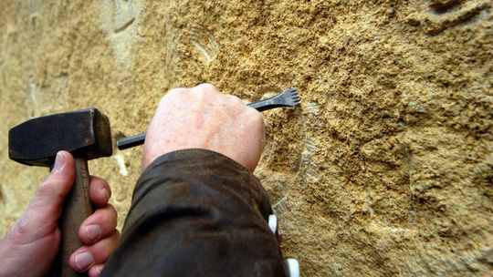 zdjęcie przedstawia pracownika, który dłutem ryje w kamieniu
