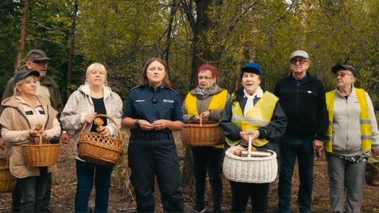 zdjęcie przedstawia grupę starszych osób w żółtych kamizelkach, wśród nich stoi policjantka, w tle są drzewa