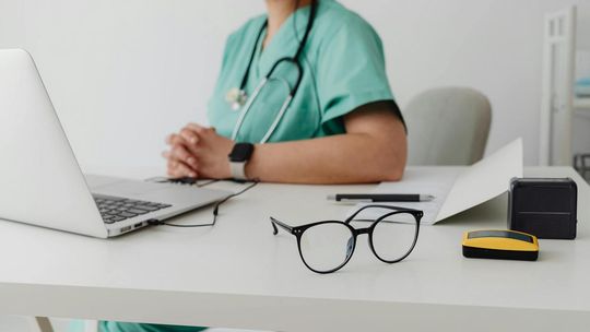 zdjęcie przedstawia okulary i lekarza za biurkiem