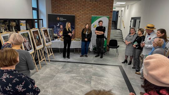 zdjęcie przedstawia kilka osób w pomieszczeniu wypełnionym portretami na sztalugach