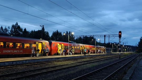 zdjęcie przedstawia pociąg stojący przy peronie, po nim idą pasażerowie, zdjęcie w nocy