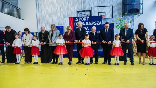 zdjęcie przedstawia grupę osób z czerwoną wstęgą