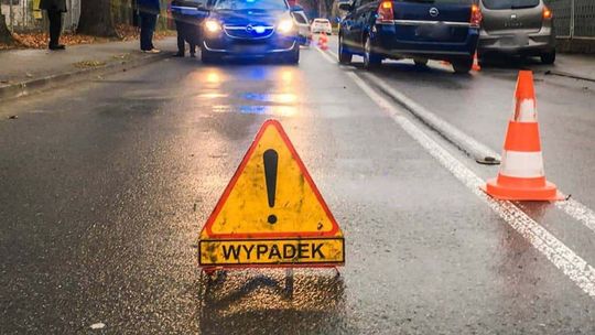 żółty trójkąt z napisem „wypadek” w tle niebieskie światła radiowozu i pojazdy na drodze