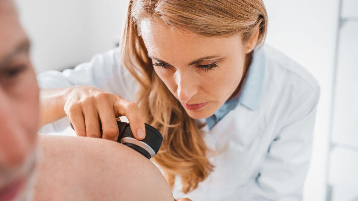 zdjęcie przedstawia kobietę w kitlu patrzącą przez lupę na ciało pacjenta